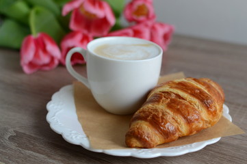 cup of cappuccino and yummy croissant with flowers