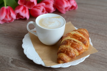 cup of cappuccino and yummy croissant with flowers