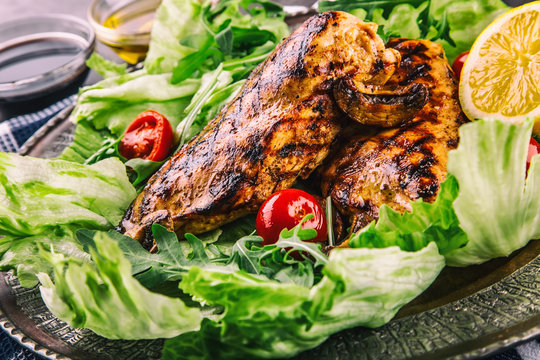 Grilled chicken breast in different variations with lettuce salad cherry tomatoes .mushrooms herbs cut lemon on a wooden board or teflon pan. Traditional cuisine. Grill kitchen.