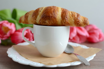 cup of cappuccino and yummy croissant with flowers