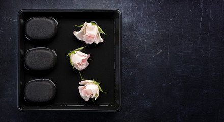 Spa composition. Rose flowers and zen stones on black background