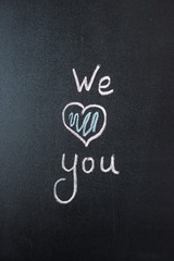 We Love You. Handwritten message on a chalkboard with an illustrated heart used as a symbol of love in this Valentines message.
