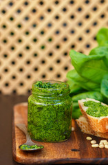 Fresh homemade Basil pesto with pine nuts in a glass jar , Basil leaf and toast on the table. Selective focus
