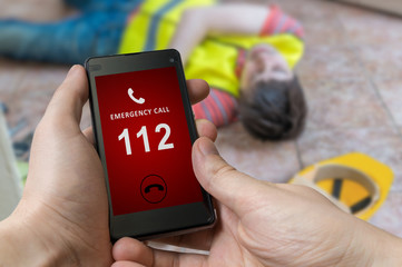 Man dialing emergency (112 number) on smartphone. Injured worker had accident and is lying on the floor. - obrazy, fototapety, plakaty