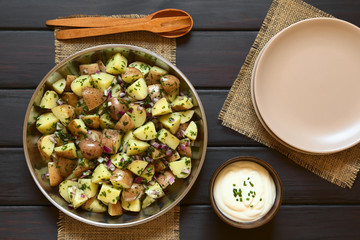 Salad of jacket potato, red onion and herbs with sour cream and plates on the side, photographed overhead on dark wood with natural light