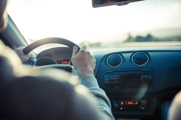 Man driving car, hand on steering wheel, looking at the road ahead.