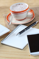 Cup of coffee on saucer with notebook on wooden table