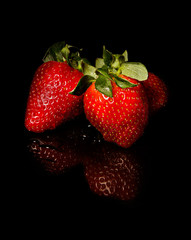 Strawberries on black, reflective background.