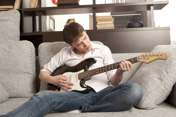 Young man with electric guitar on sofa