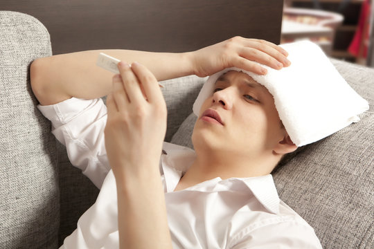 Sick young man lying on sofa checking his temperature