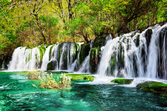 Waterfall and azure lake with crystal water among green woods