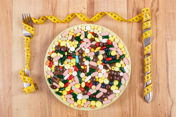 Tablets or supplements on plate and fork with knife wrapped centimeter, health care and slimming concept