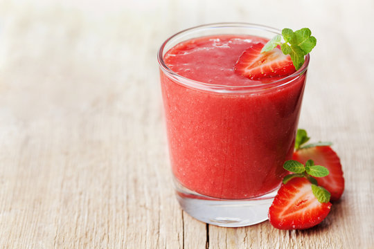 Strawberry smoothie in a glass decorated with mint leaves on rustic background, fresh fruit juice is red, detox food, diet and healthy breakfast