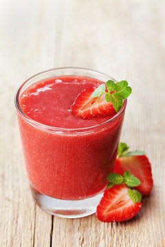 Strawberry smoothie in a glass decorated with mint leaves on rustic background, fresh fruit juice is red, detox food, diet and healthy breakfast
