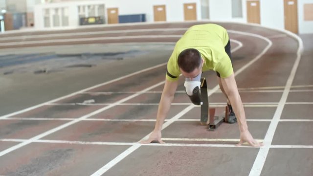 Young confident athlete with prosthetic leg starting running from blocks in slow motion