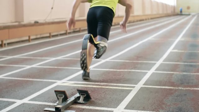 Rear view of athlete with prosthetic leg launching from starting blocks in slow motion. Perfect for sports, motivation, inclusivity, fitness, inspirational visuals