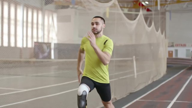 Paralympic athlete with prosthetic leg running on track in practice, slow motion 