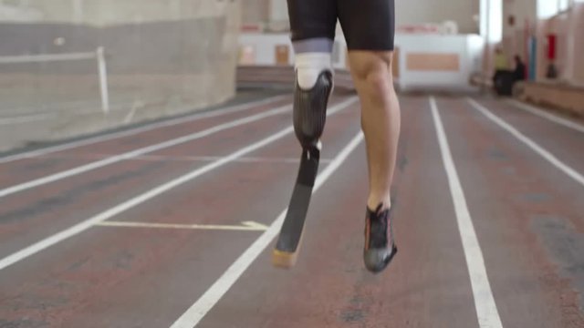 Low section of sportsman with artificial leg practicing jumping exercise on track at indoor stadium. Perfect for sports, fitness, Paralympics, motivation, inclusive athletic visuals