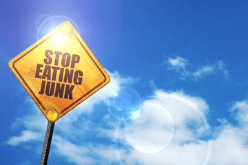 Yellow road sign with a blue sky and white clouds: stop eating j