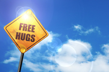 Yellow road sign with a blue sky and white clouds: free hugs