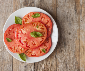 Tomatoes with basil in white plate on wooden table background. 