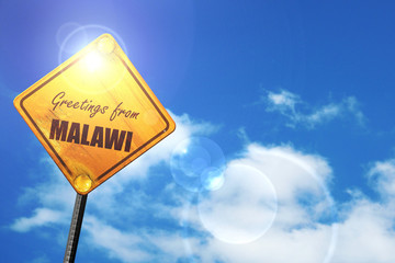 Yellow road sign with a blue sky and white clouds: Greetings fro