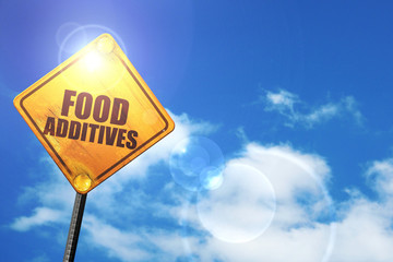 Yellow road sign with a blue sky and white clouds: food additive
