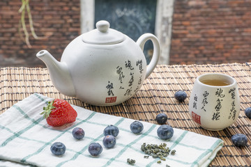 Teapot with cup of tea on the woven mat with some blueberries and strawberry