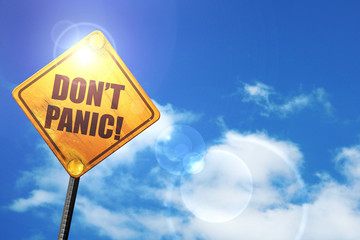 Yellow road sign with a blue sky and white clouds: don't panic