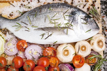 Fresh sea fish against a dark background. Sea fish with fragrant herbs, fresh vegetables, sea coarse salt and spices.