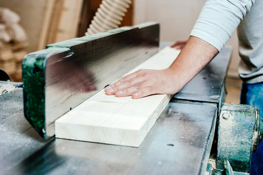 Detail of carpenter hands on a wooden plank on a woodworking machinery factory.
