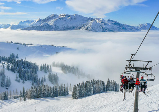 Alpine ski slope mountain winter panorama with ski lift,skiers and snow covered forest.