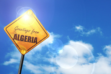 Yellow road sign with a blue sky and white clouds: Greetings fro
