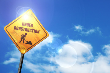 Yellow road sign with a blue sky and white clouds: Under constru