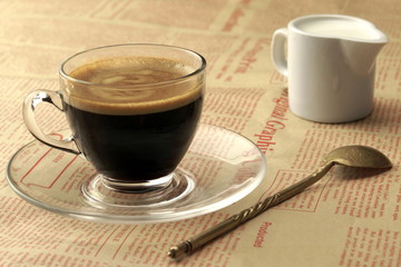 Transparent Coffee Cup With Espresso, Cream And Spoon On Newspap
