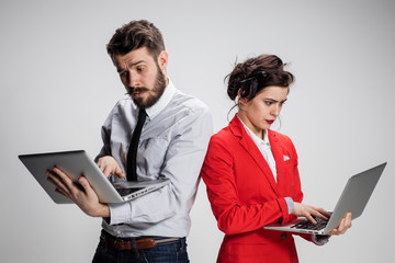 The young businessman and businesswoman with laptops  communicating on gray background
