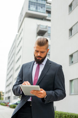 Naklejka na ściany i meble Young bearded businessman writting business e-mail using his tab