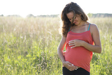 Young beautiful pregnant woman holding tummy smiling, in red a light summer dress, happy