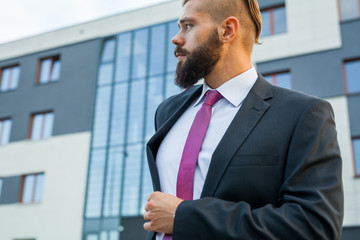 Young attractive businessman ajusting jacket. Outdoor photo.