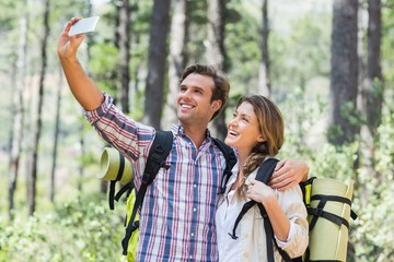 Smiling couple clicking selfie while standing in forest 