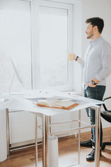 Young man in a modern office design sketching construction project design in a note book computer and drinks coffee