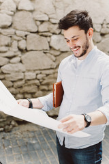Obraz premium Young smiling man outdoor potrait holding sketching construction project in his hands 