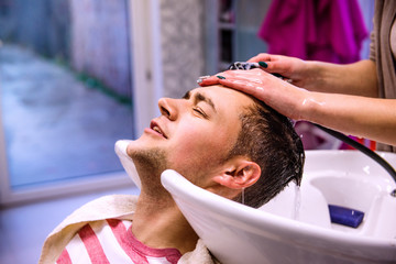 Professional hairdresser washing hair to her handsome client.