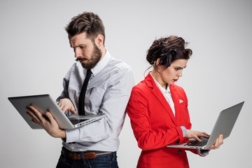 The young businessman and businesswoman with laptops  communicating on gray background