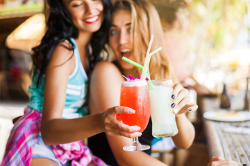 Two trendy cool hipster girls, friends, the blonde and the brunette drink cocktails at the cafe on...