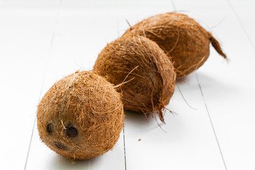 Three whole not split coconuts, on a wooden white plank background. Some coconuts in the group.