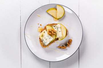 Sandwich with Blue cheese with slices of pear, nuts and honey on plate.  Flat lay, center.