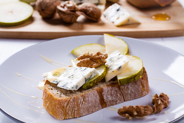 Sandwich with Blue cheese with slices of pear, nuts and honey on plate.