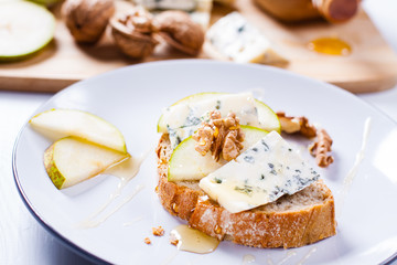 Sandwich with Blue cheese with slices of pear, nuts and honey on plate.