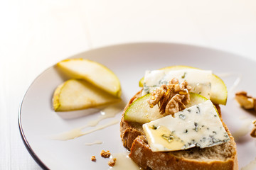 Sandwich with Blue cheese with slices of pear, nuts and honey on plate.